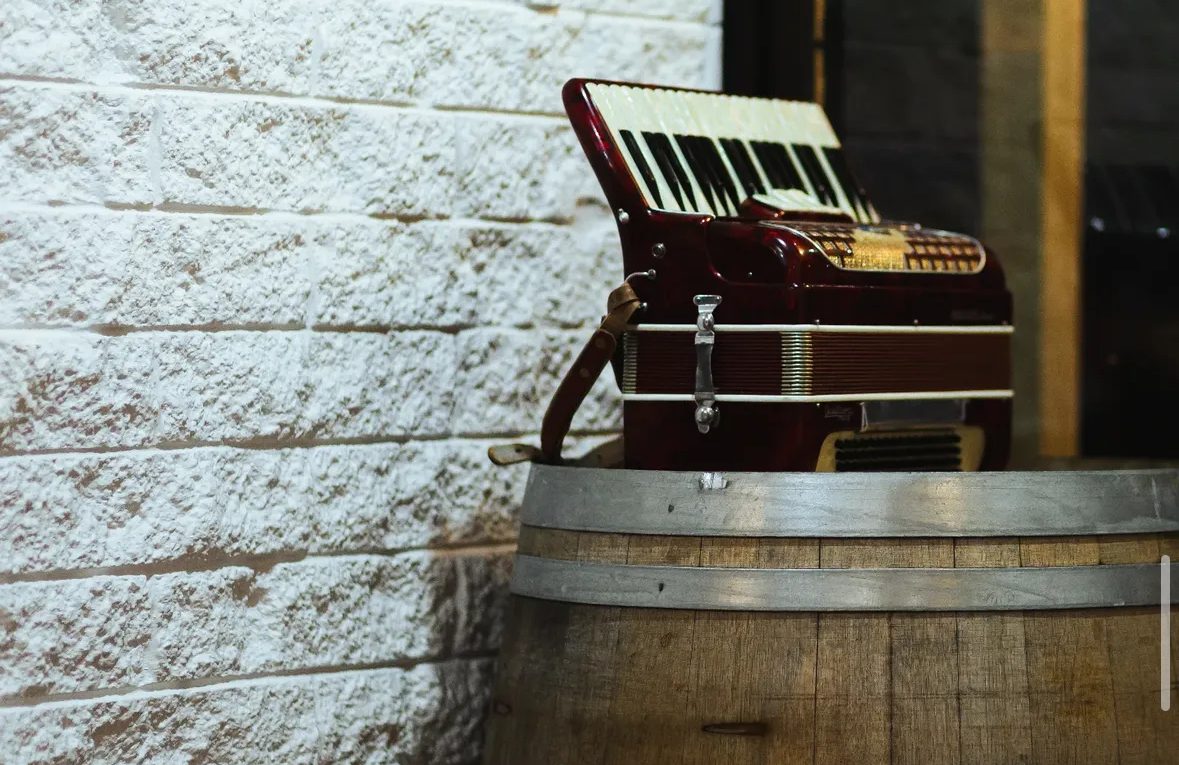 A red accordion resting on an oak barrel against a whitewashed stone wall